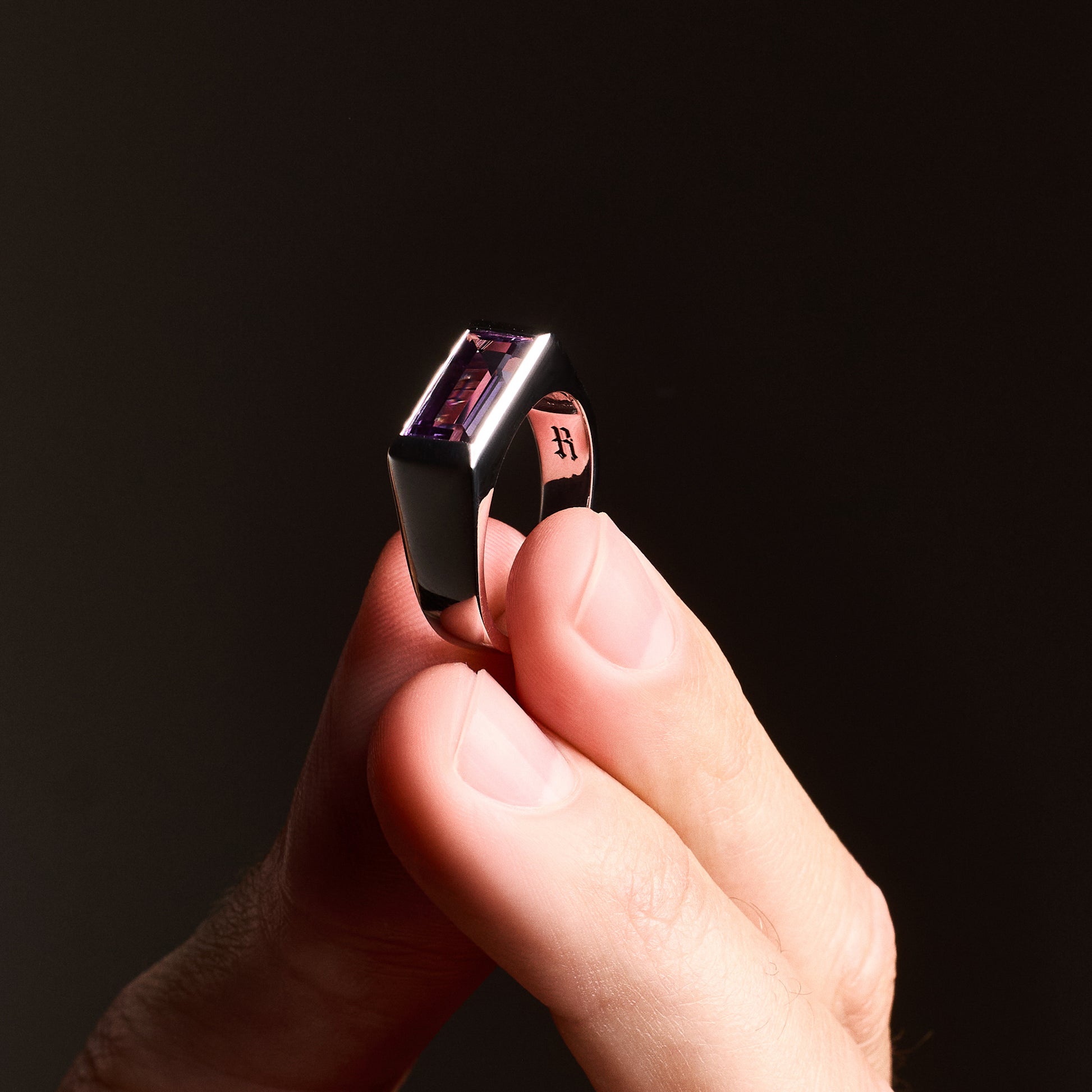 Close-up of a person holding the Amethyst Ring, highlighting the natural baguette-cut amethyst stone set in a high-polish silver rhodium-plated setting.