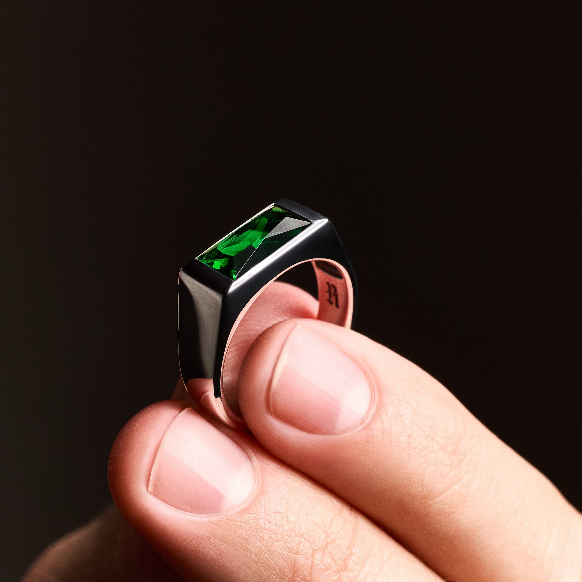 Close-up of a person holding the Emerald Signet Ring, showcasing the green baguette-cut glass stone set in rhodium-plated sterling silver.