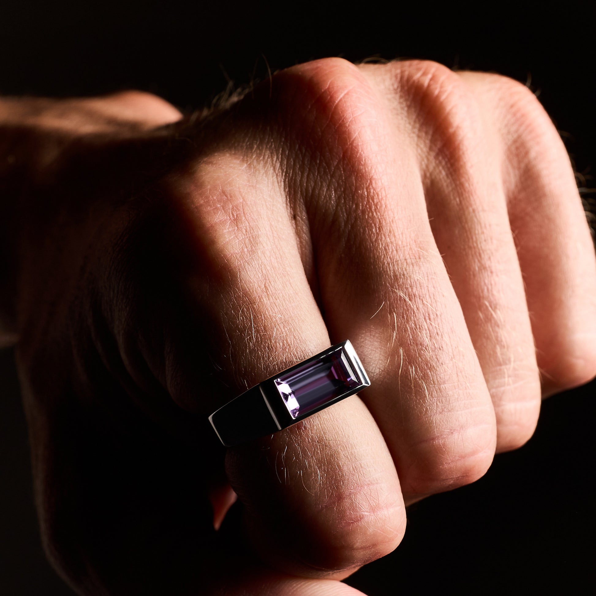 Close-up of a person wearing the Amethyst Ring, showcasing a natural baguette-cut amethyst stone set in a high-polish silver rhodium-plated setting.