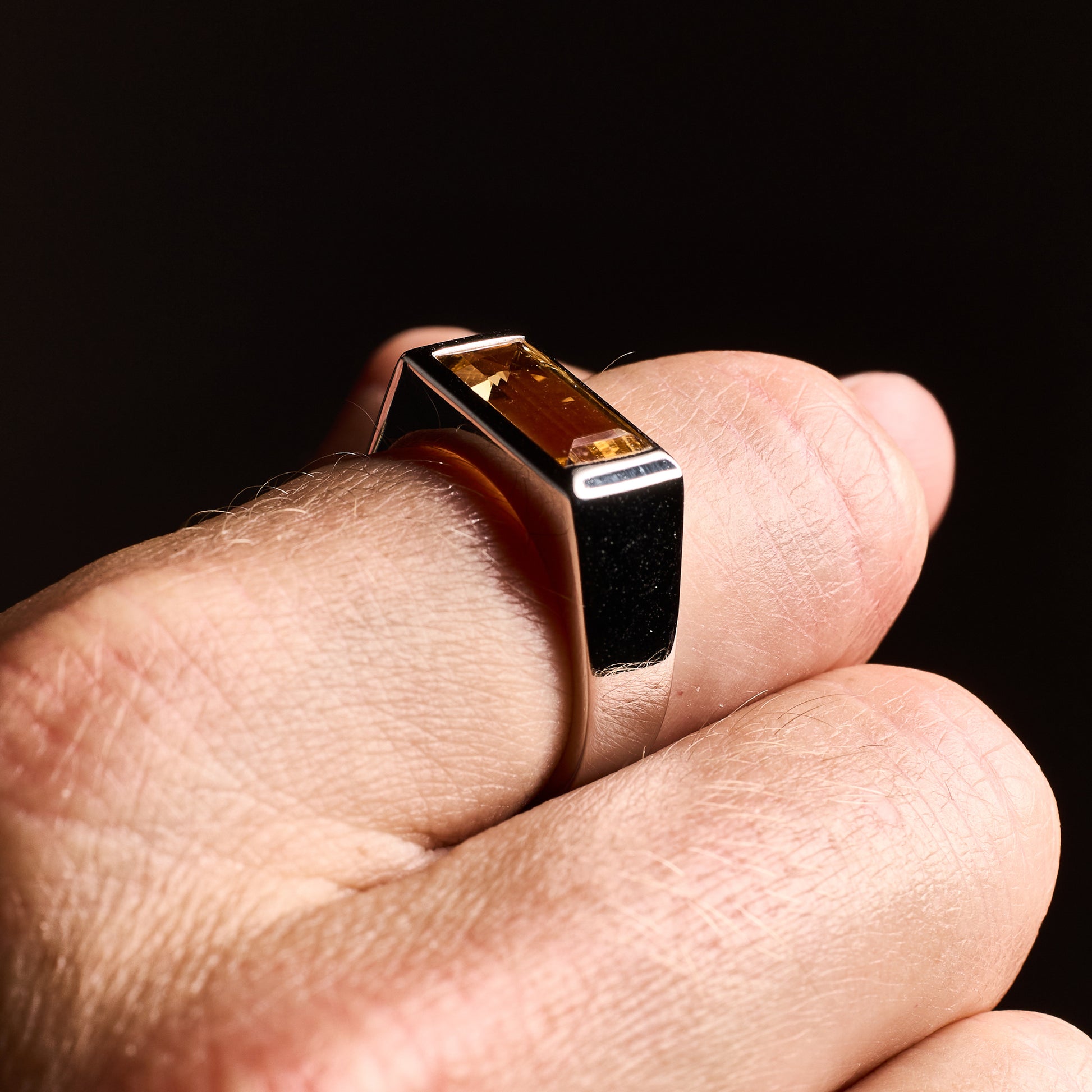 Close-up of a man wearing the Citrine Signet Ring with a natural baguette-cut citrine stone set in high-polish rhodium-plated sterling silver.