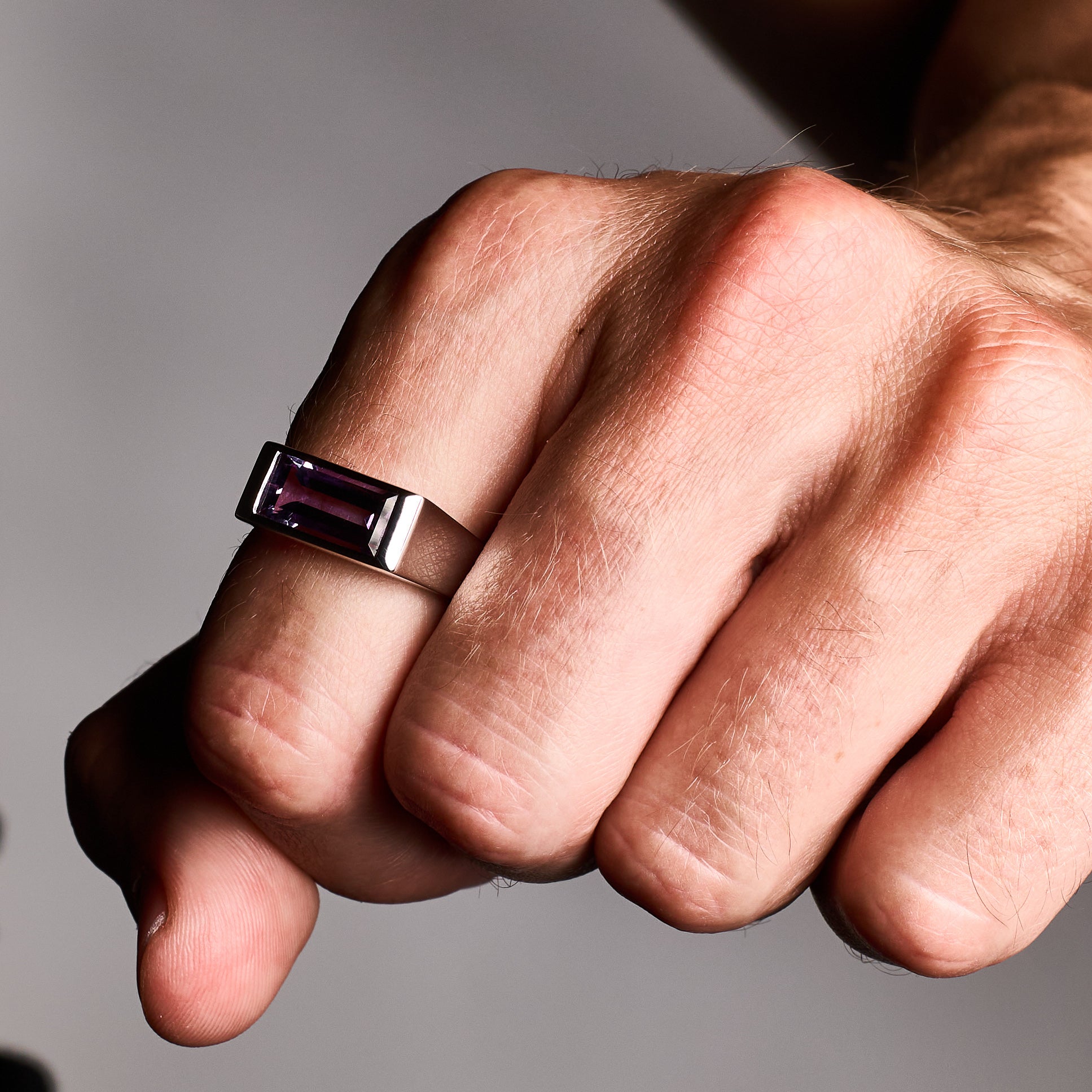 Close-up of a person wearing the Amethyst Ring, showcasing a natural baguette-cut amethyst stone set in a high-polish silver rhodium-plated setting.