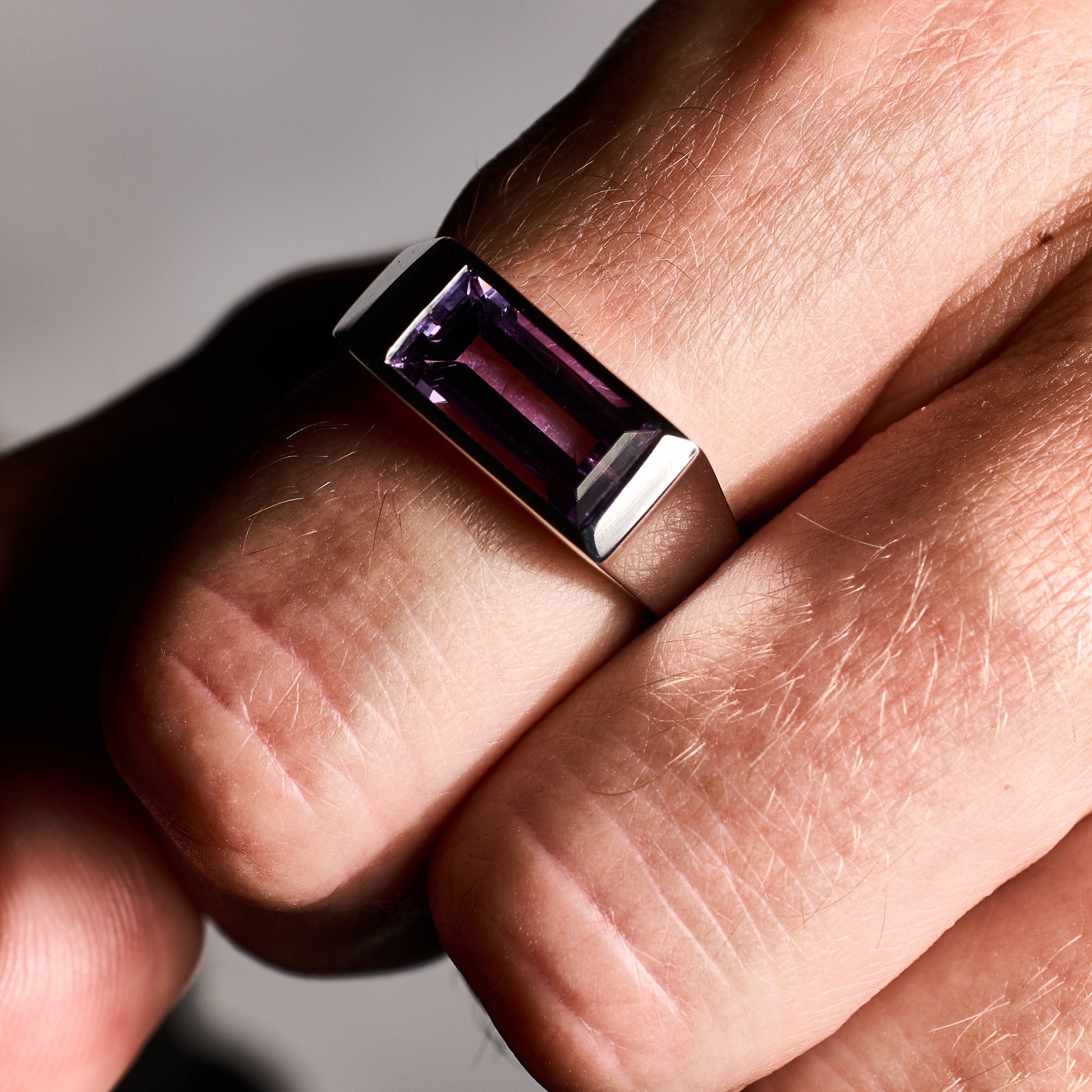 Close-up of a person wearing the Amethyst Ring, showcasing a natural baguette-cut amethyst stone set in a high-polish silver rhodium-plated setting.