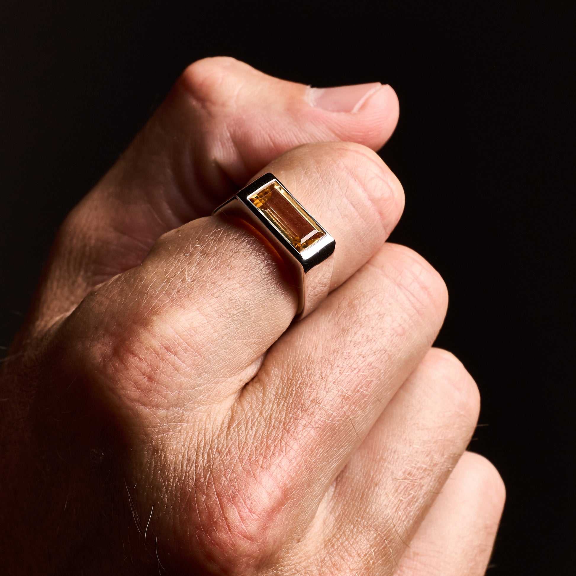 Close-up of a man wearing the Citrine Signet Ring with a natural baguette-cut citrine stone set in high-polish rhodium-plated sterling silver.